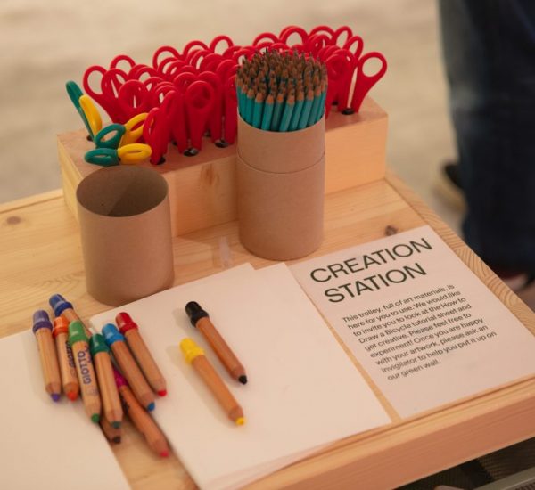 A wooden table labeled “CREATION STATION” holds colored pencils, scissors, and blank paper for interactive activities.