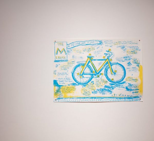 A hand-drawn artwork of a bicycle in blue and yellow is displayed on a white wall, surrounded by handwritten notes and sketches.