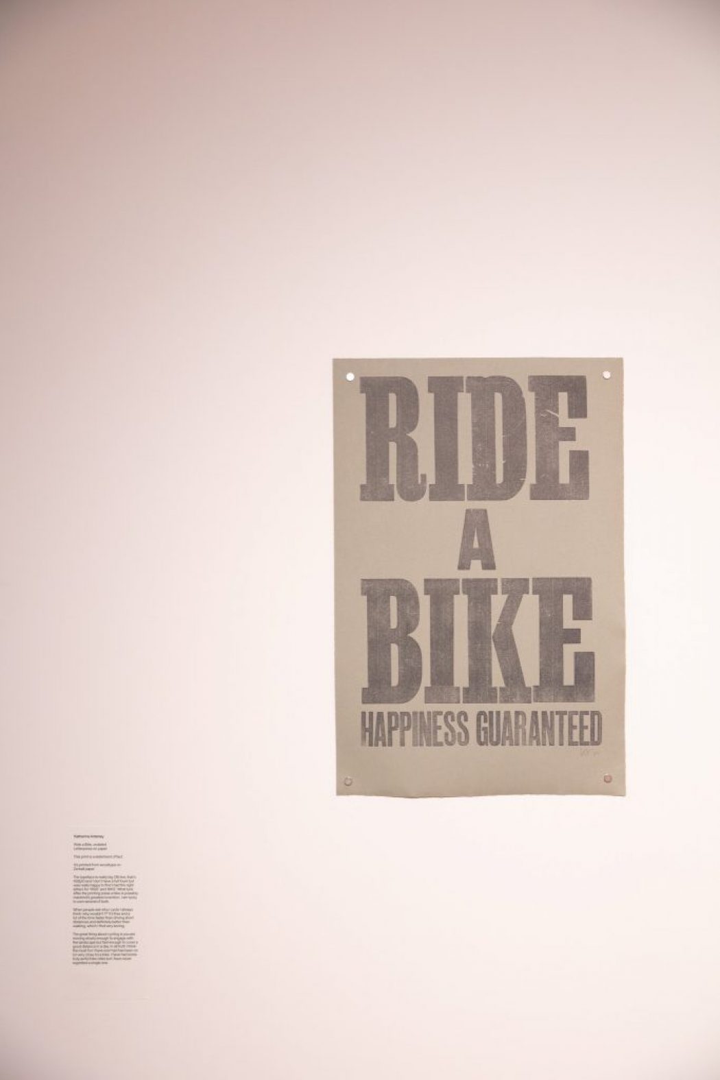 A poster with bold text reads “RIDE A BIKE HAPPINESS GUARANTEED” on a plain wall.