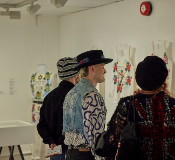 A gallery room features rows of mannequins dressed in patterned garments, creating a corridor-like view. Exhibition signage for “Collecting Sue Clowes” is visible in the background.