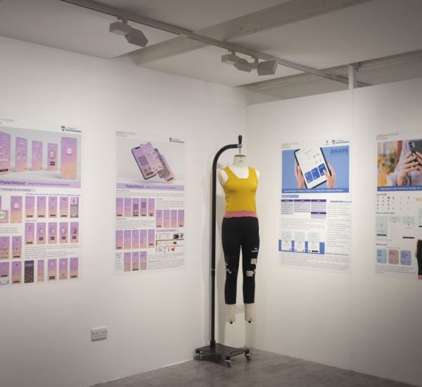 A gallery display features large posters on white walls showcasing app interface designs and informational graphics, primarily in purple and blue tones. In the center, a mannequin dressed in a yellow crop top and black leggings stands on a metal stand.
