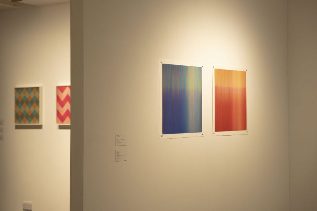 Two abstract gradient paintings, one in blue-green and the other in red-orange, are displayed side by side on a white gallery wall.