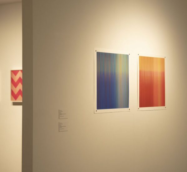 Two abstract gradient paintings, one in blue-green and the other in red-orange, are displayed side by side on a white gallery wall.