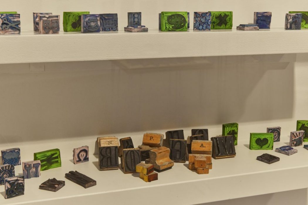 Shelves hold an assortment of small, colorful blocks featuring intricate designs and letters. Some of the blocks appear to be wooden letterpress pieces.