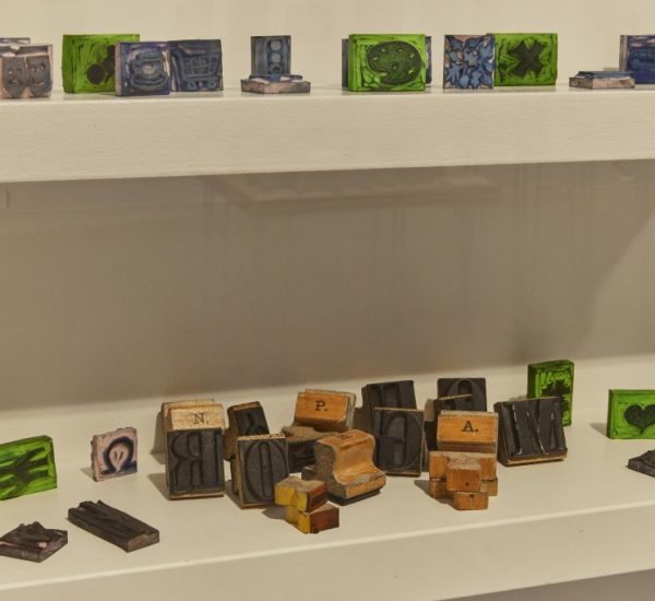 Shelves hold an assortment of small, colorful blocks featuring intricate designs and letters. Some of the blocks appear to be wooden letterpress pieces.