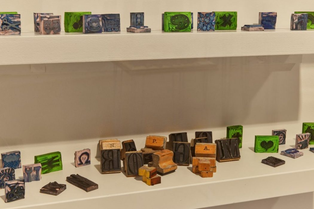 Shelves hold an assortment of small, colorful blocks featuring intricate designs and letters. Some of the blocks appear to be wooden letterpress pieces.