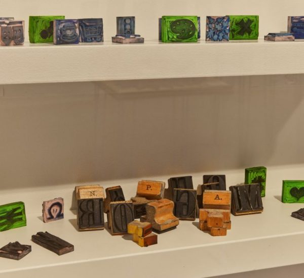 Shelves hold an assortment of small, colorful blocks featuring intricate designs and letters. Some of the blocks appear to be wooden letterpress pieces.
