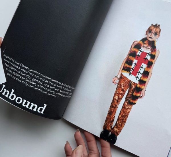 The image shows an open magazine with text on the left page and a fashion photograph on the right. The photograph features a person wearing a sleeveless top with a bold red cross design, a furry striped vest, and patterned trousers.
