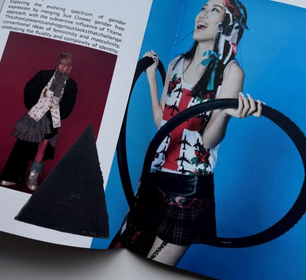 The image shows an open magazine with text on the left page titled “Titane” and a fashion photograph on the right. The photograph features a person wearing a sleeveless patterned top, a short skirt, and holding two large black hoops against a bright blue background.
