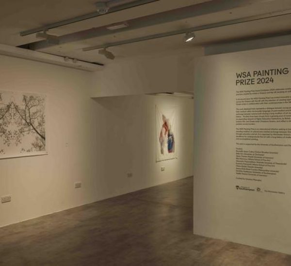 A gallery wall displays the WSA Painting Prize 2024 text alongside two artworks: one featuring delicate tree branches and another with abstract colorful forms. The space is softly lit with neutral walls and a polished floor.