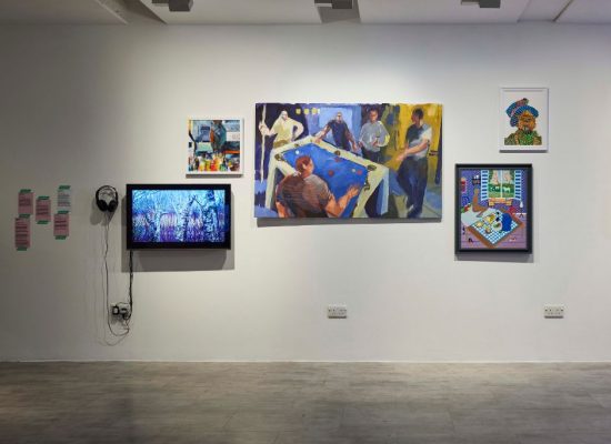 A gallery wall displays multiple artworks, including paintings of people around a table, framed illustrations, and a monitor with headphones attached. The arrangement combines vibrant colors and mixed media pieces.