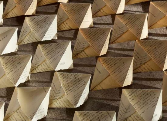 A close-up view of many folded paper forms arranged in a grid-like pattern on the floor. The papers create repeating geometric shapes with visible text on each fold.