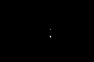 A dark scene features a bright white circular ring of light on the floor, with two small points of light hovering above it in the background. Most of the space is unlit, emphasising the glowing ring against the black surroundings.