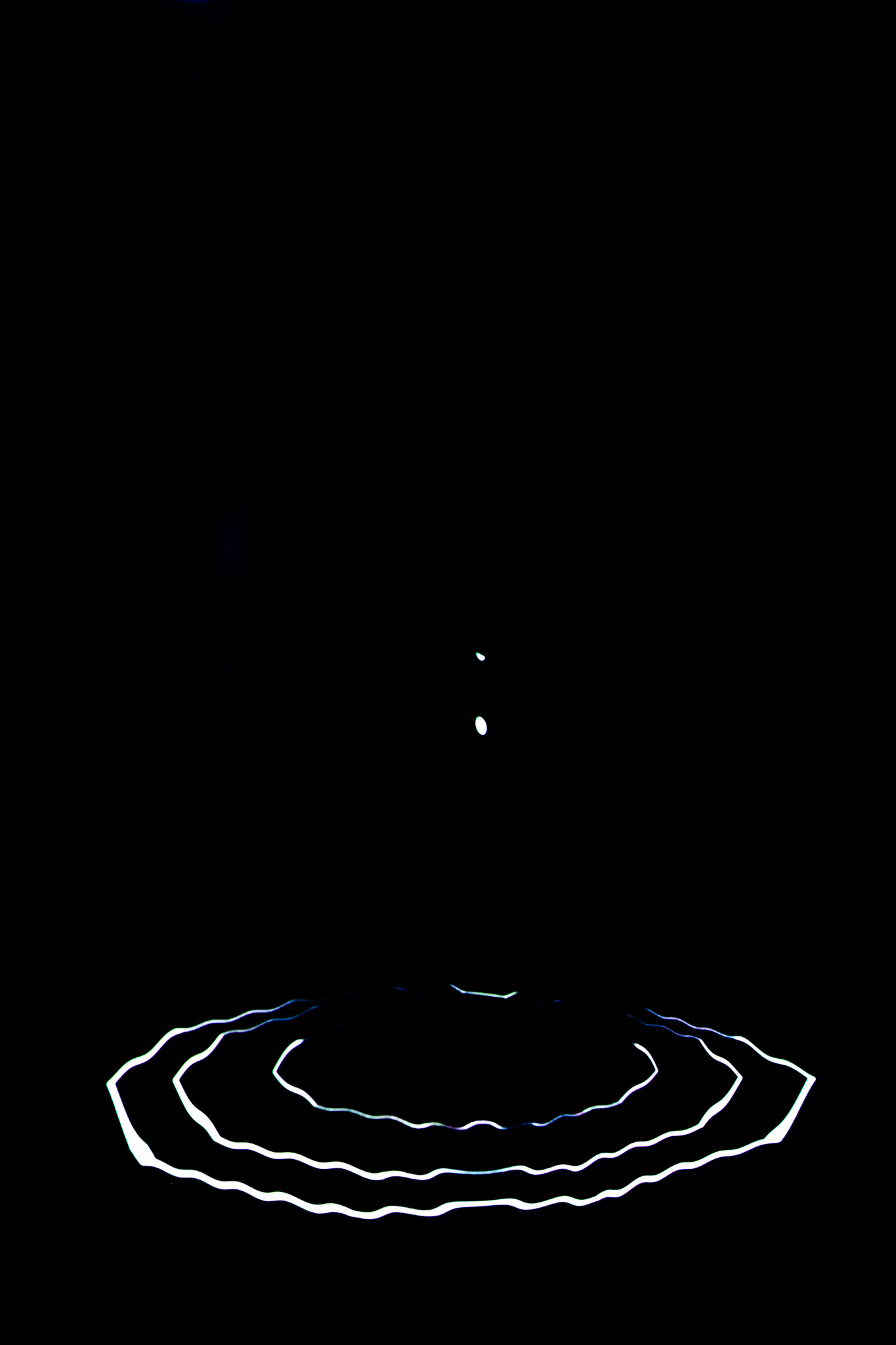 A dark scene features a bright white circular ring of light on the floor, with two small points of light hovering above it in the background. Most of the space is unlit, emphasising the glowing ring against the black surroundings.