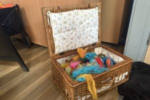 An open wicker basket contains colourful wool fibres used for a felting workshop. The materials are arranged indoors ready for participants to use.