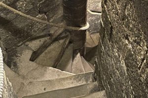 Narrow stone spiral staircase winding through the interior of a bell tower. The worn steps curve tightly around a central column.