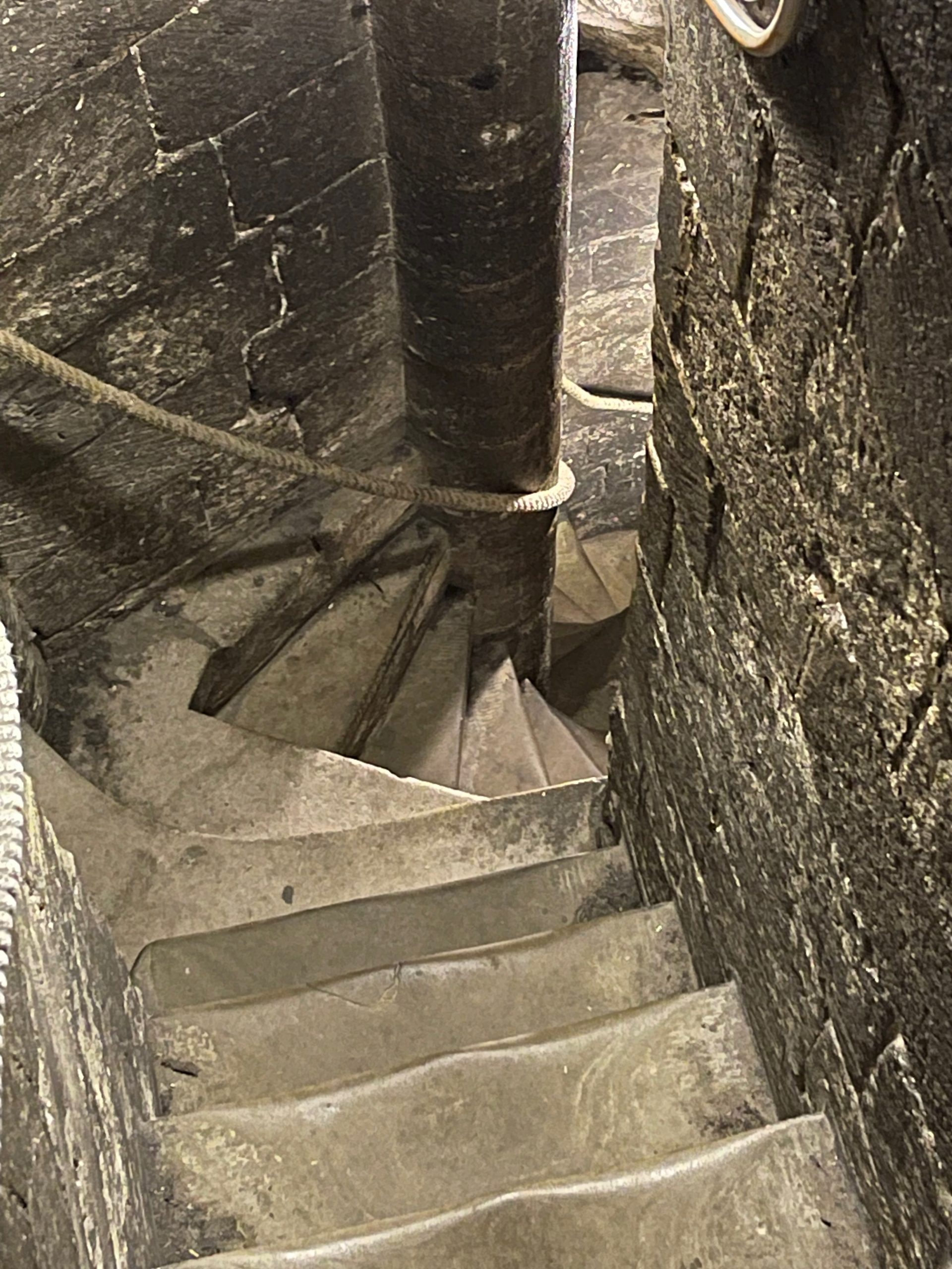 Narrow stone spiral staircase winding through the interior of a bell tower. The worn steps curve tightly around a central column.