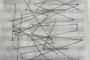 Abstract line drawing on transparent paper over musical staves, with black lines crossing and intersecting to create a graphic score-like composition.